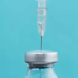 A hypodermic needle drawing liquid from a bottle