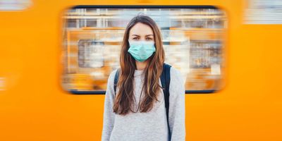 Woman with a face mask on in front of a train looking at the camera