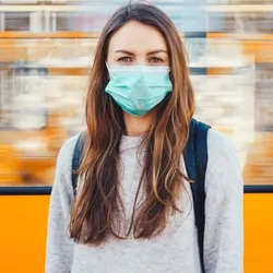 Woman with a face mask on in front of a train looking at the camera