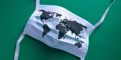 A facemask with a map of the world printed on it lying on a green backdrop