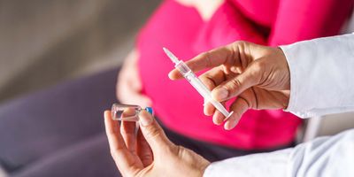 A clinical worker administers a COVID-19 vaccine to a pregnant person.