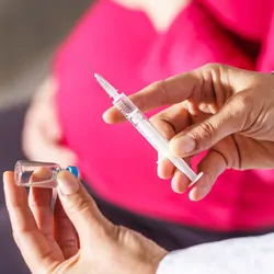 A clinical worker administers a COVID-19 vaccine to a pregnant person.