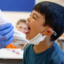Health care professional swabing a childs mouth for a saliva sample