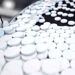 White pills being moved down a conveyor belt