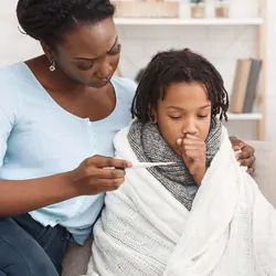Mother checking the temperature of sick child wrapped in a blancket