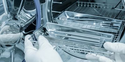 A gloved hand putting medical tools into an autoclave for sanitization