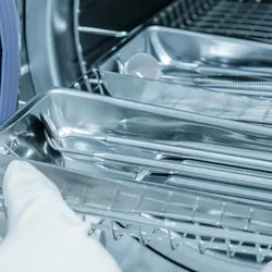 A gloved hand putting medical tools into an autoclave for sanitization