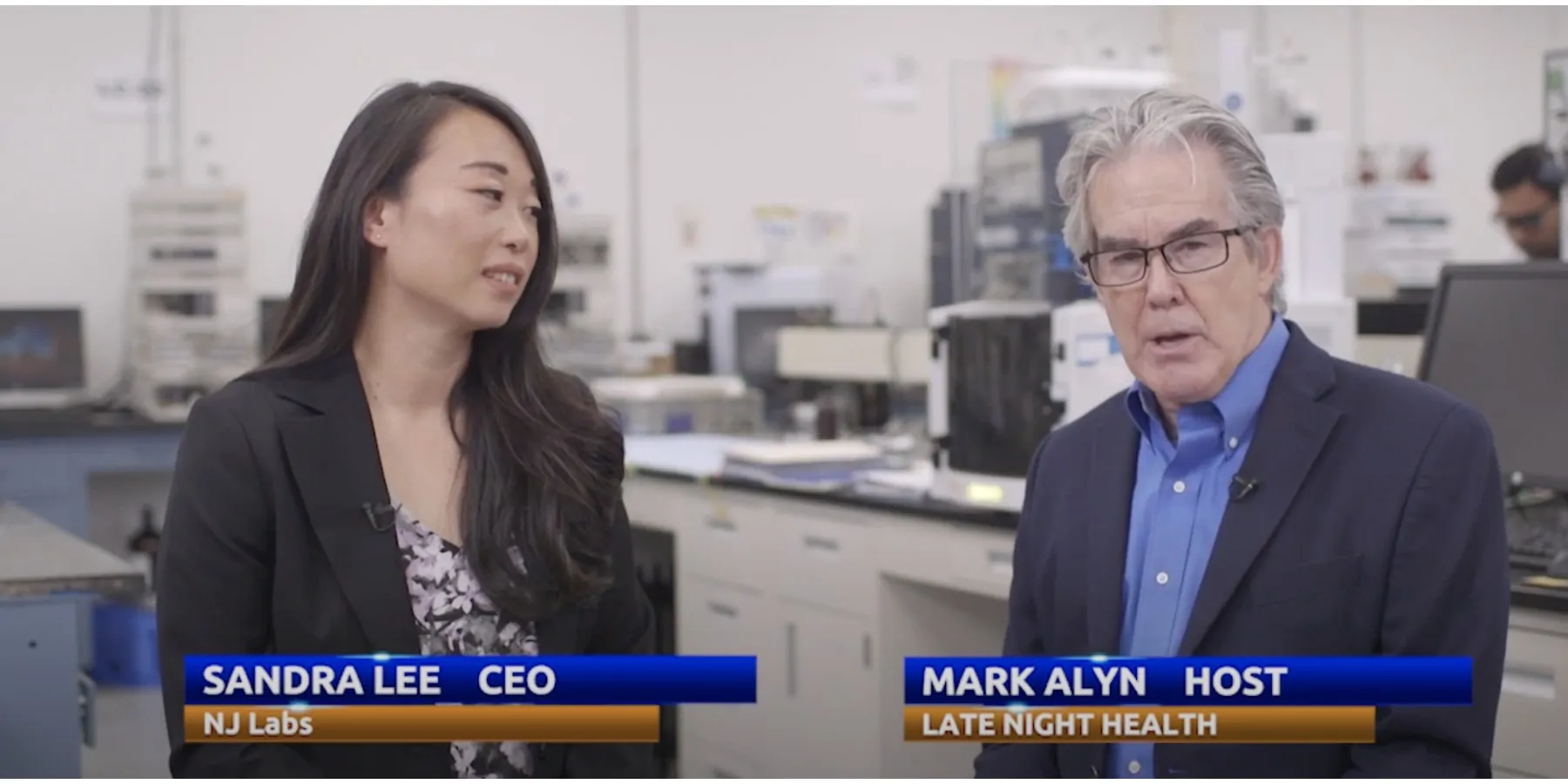 Host and co-host of the new podcast speaking to the camera with a lab in the background