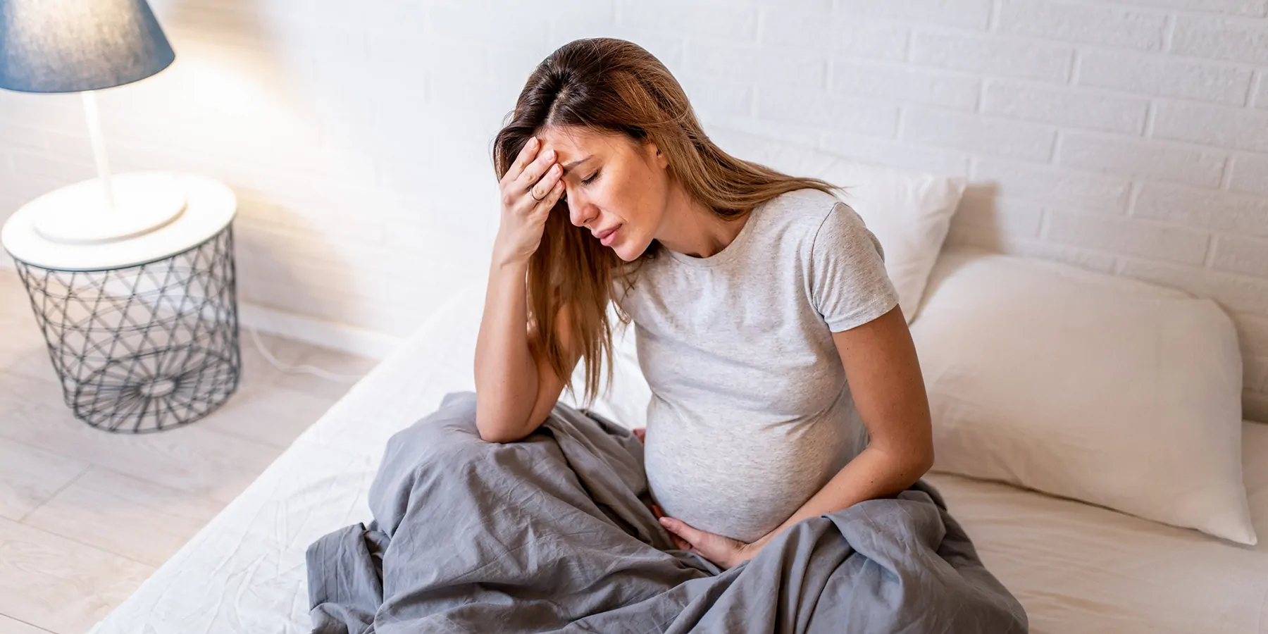 Pregnant women in bed with hands on forehead 