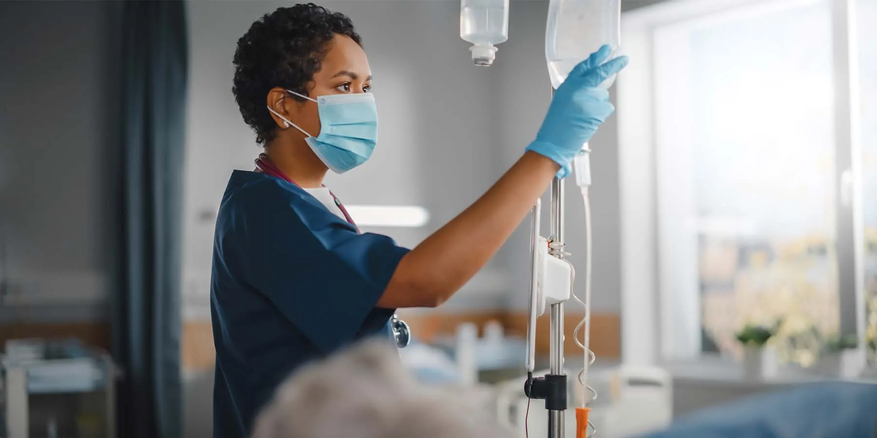Female nurse checking IV bags near a patient in a hospital bed