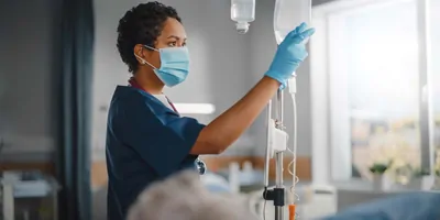 Female nurse checking IV bags near a patient in a hospital bed