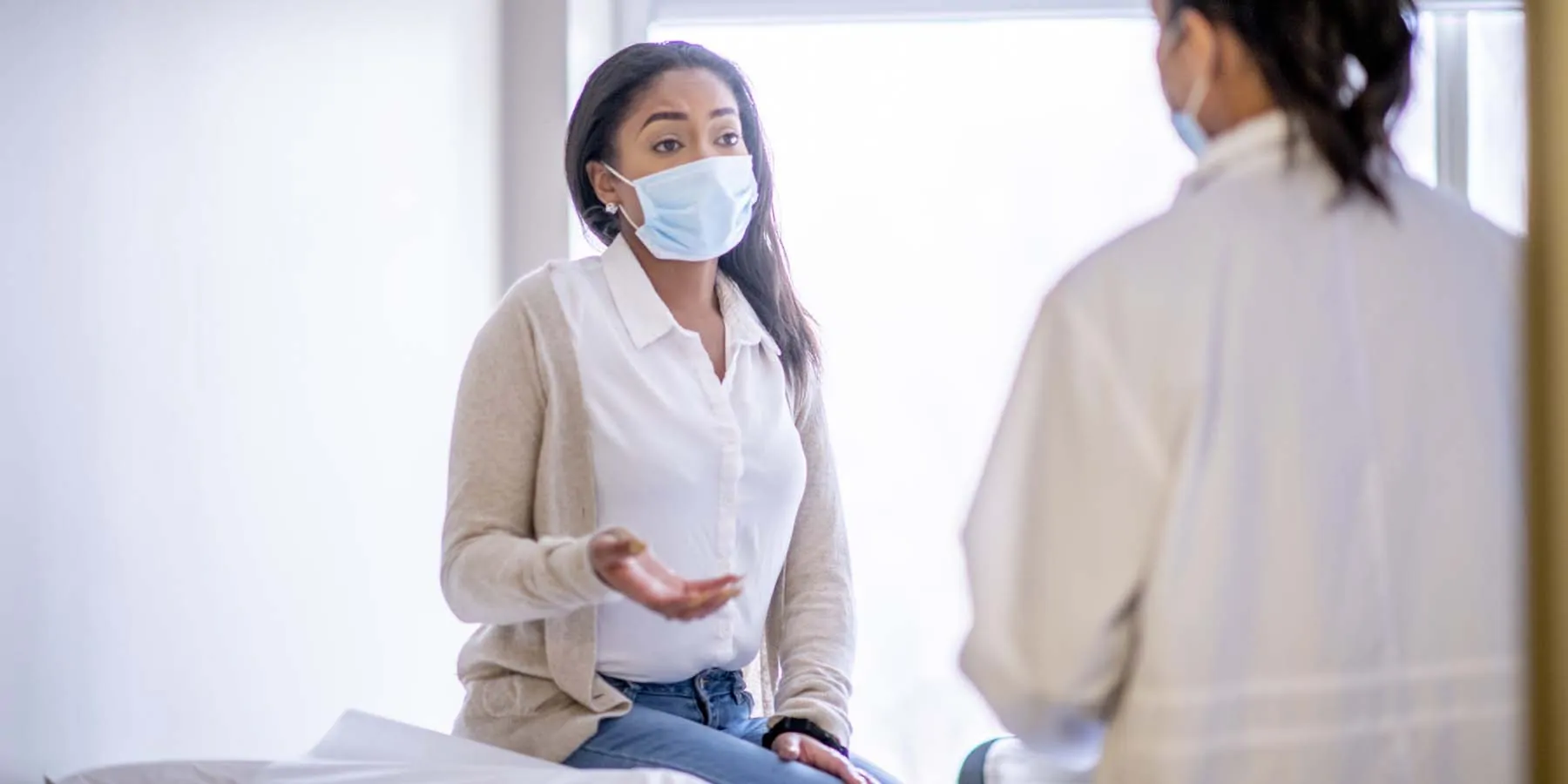 Women wearing mask, describing symptoms to a doctor