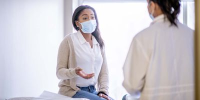 Women wearing mask, describing symptoms to a doctor