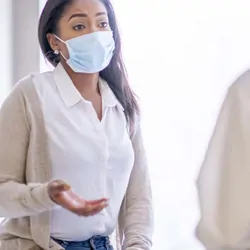 Women wearing mask, describing symptoms to a doctor