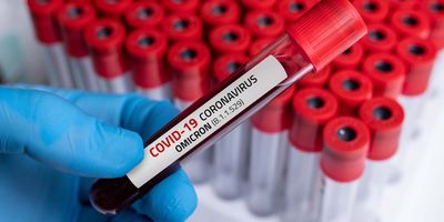 Gloved hand holding a vial ov blood labeld as being positive for Omicron variant