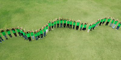 Photo of people wearing green shirts lined up outside standing on a green lawn.
