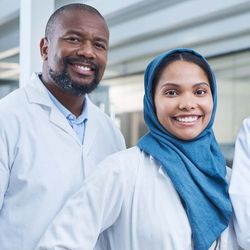 Photo of a Black man and a woman wearing a hijab wearing white lab coats in the clinical lab.