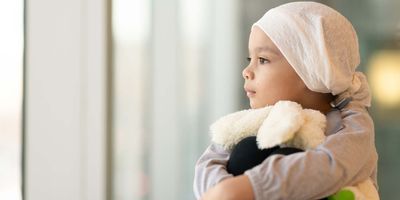 Child taking a break from cancer treatment, looking out a window with a stuffed toy