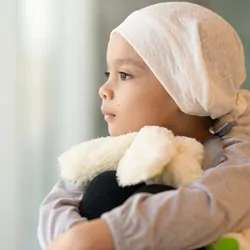 Child taking a break from cancer treatment, looking out a window with a stuffed toy
