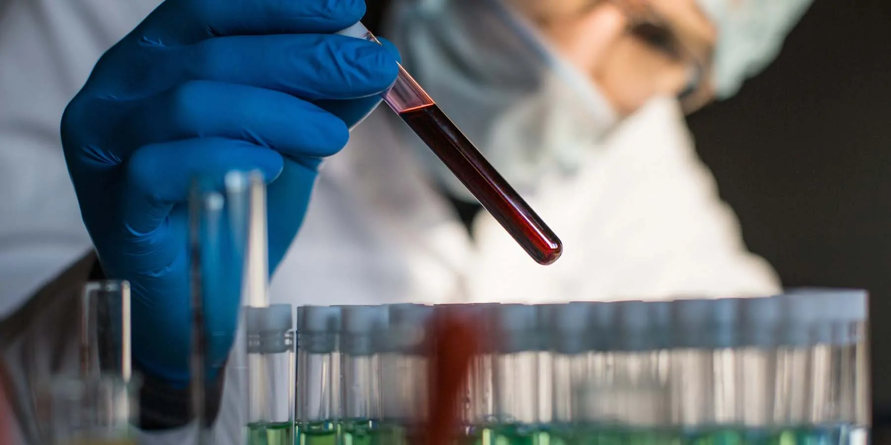 Researcher in PPE looking at a blood vial with blood