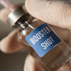 Gloved hand holding a vial labled "booster shot"