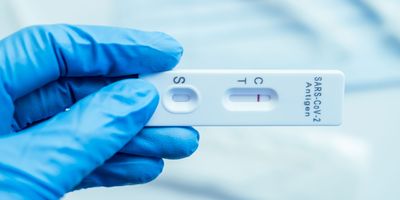 Photo of a clinical lab professional wearing gloves and holding a rapid antigen test.