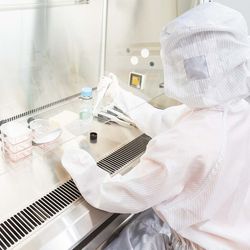 Photo of a clinical lab professional wearing PPE working with COVID-19 samples in a biosafety cabinet.