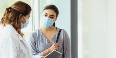 Female researcher wearing a mask and speaking with another women 