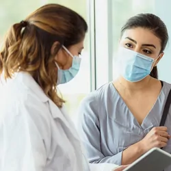 Female researcher wearing a mask and speaking with another women 