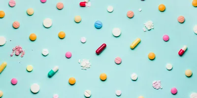 Photograph of different pills and pharmaceuticals spaced out in a grad on a blue background.