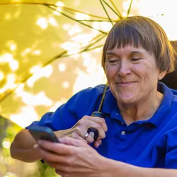 Woman with MS in wheelchair carries an umbrella for the sun and looks hopeful for a cure for MS.