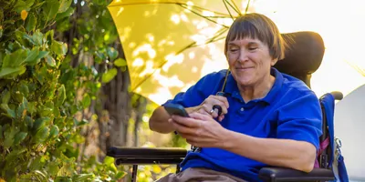 Woman with MS in wheelchair carries an umbrella for the sun and looks hopeful for a cure for MS.
