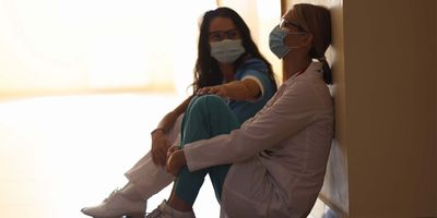 Photograph of two health care workers sitting in masks in a corridor, coping with the high stress of providing health care in Ukraine during the Russian invasion. 