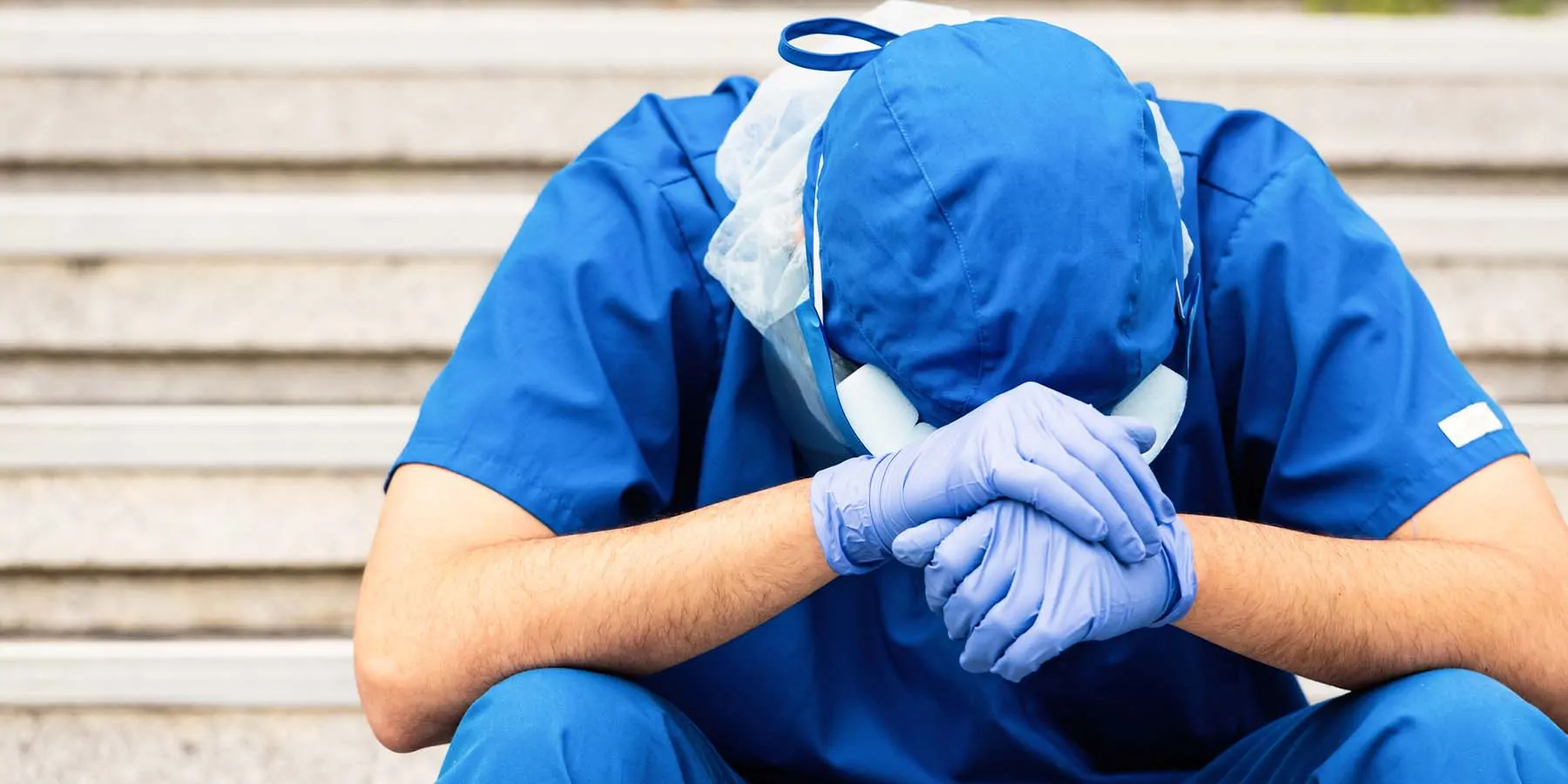 Health care provider in PPE head in hands, sitting down on steps, stressed