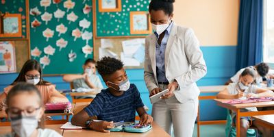Teacher helping student at their desk, grade 6-8, students and teacher wearing masks
