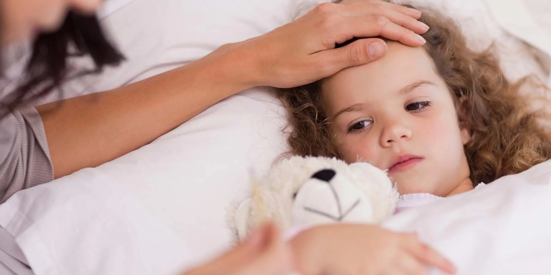 Young girl, sick in bed with mother checking her temperature
