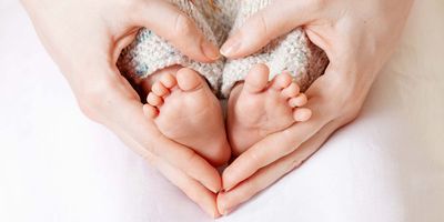 Mother's hands around her childs feet making a heart shape