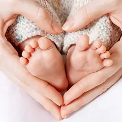 Mother's hands around her childs feet making a heart shape
