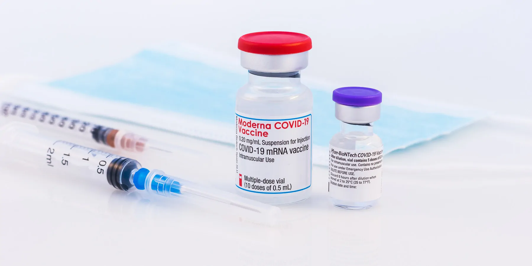 Vaccine vials next to two needles and face masks