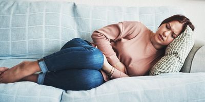 Photograph of a young woman lying on the sofa, suffering from abdominal pain due to fibroids. 