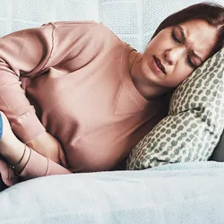 Photograph of a young woman lying on the sofa, suffering from abdominal pain due to fibroids. 