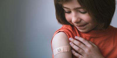 Young girl smiling with bandaged arm after getting vaccinated