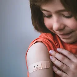 Young girl smiling with bandaged arm after getting vaccinated