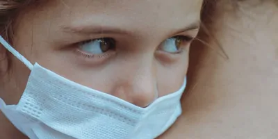 Young girl wearing face mask held in mothers arms