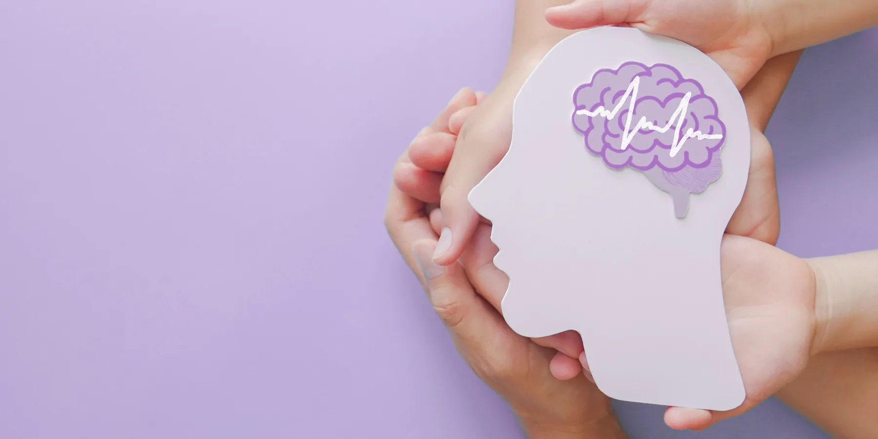 Hands holding a cut out of a human head in profile, with a paper brain on a pink background