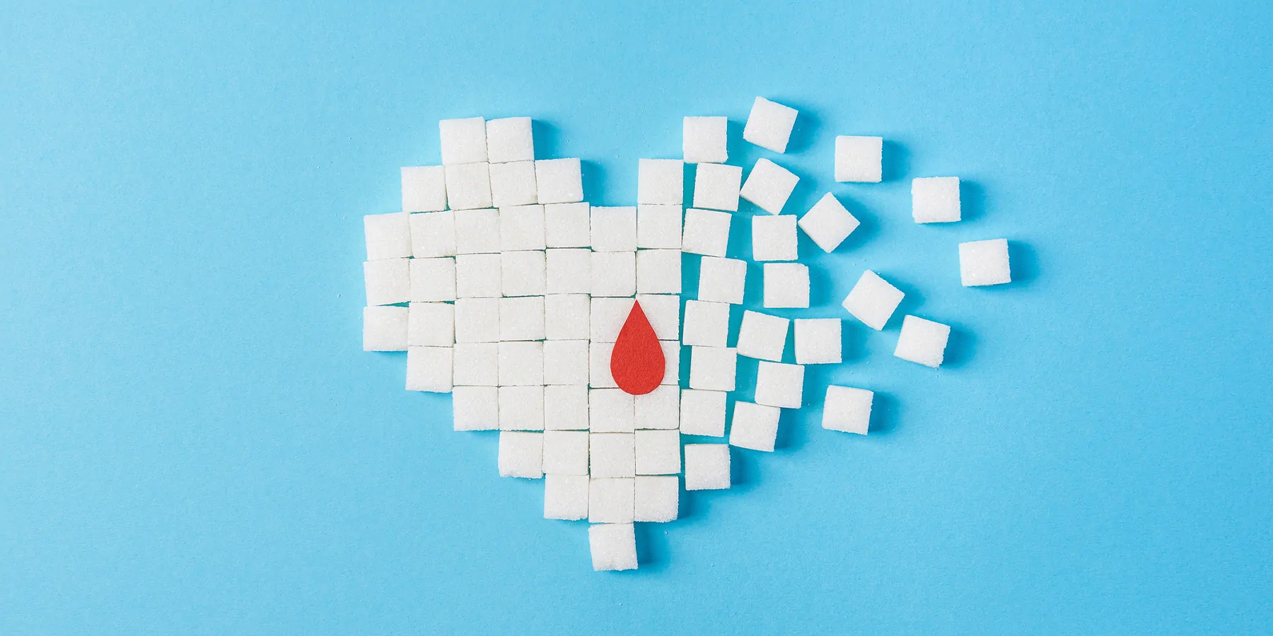 A heart made of sugar cubes on a blue background with a paper blood drop in the center