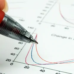 Researcher following a graph line from a scientific paper with a pen
