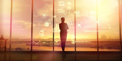 A clinical industry professional wearing a suit stands in front of a large window looking at a sunset.