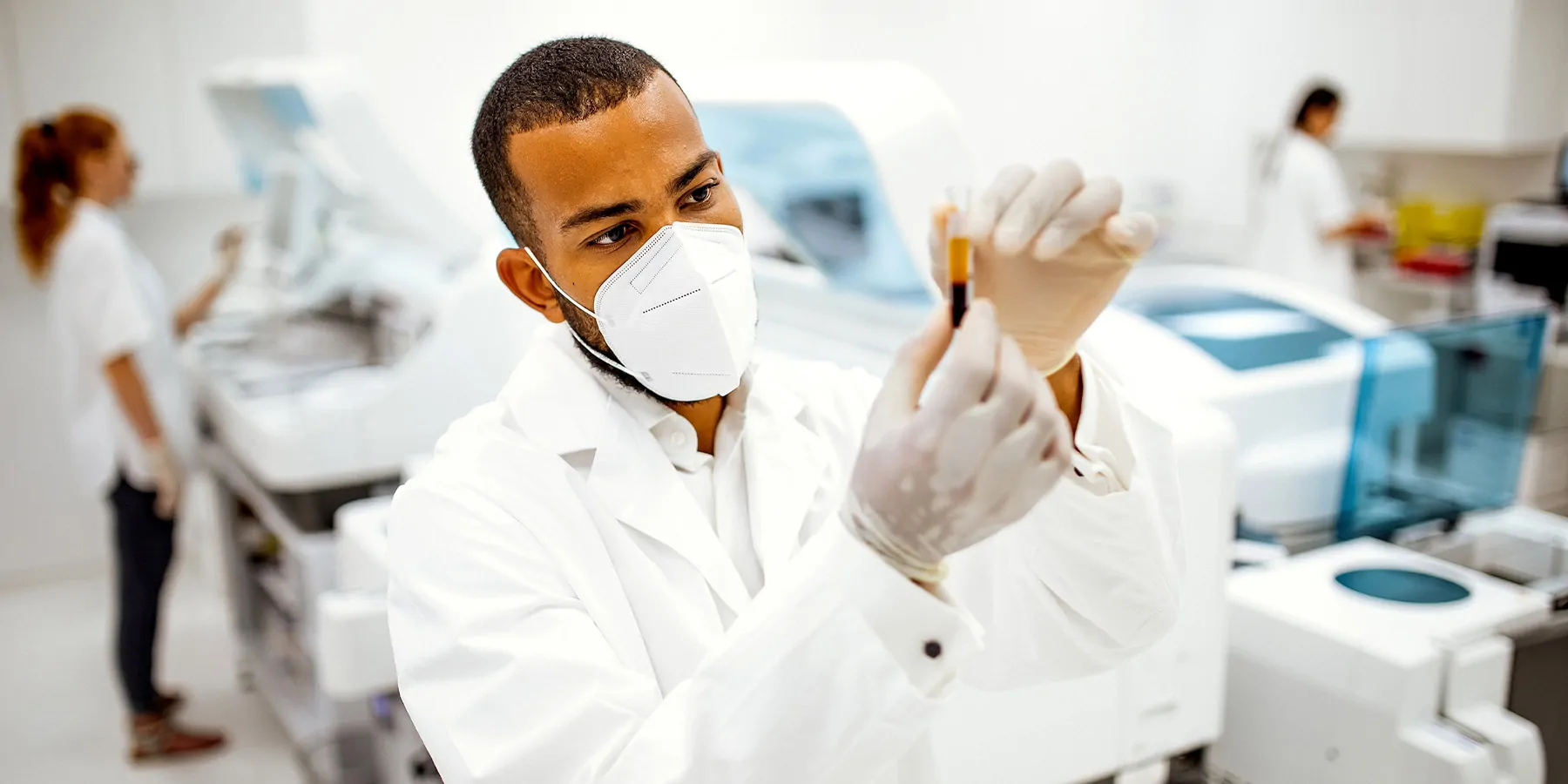 Scientist working in a lab wearing a mask and looking at a blood sample
