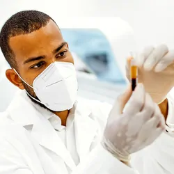 Scientist working in a lab wearing a mask and looking at a blood sample